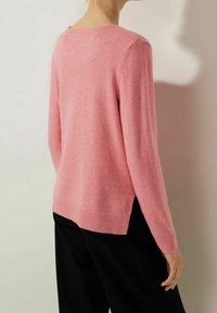 Rosa stickad tröja med rund hals, långa ärmar, ribbad nederkant och sidofickor, som erbjuder en mjuk textur och avslappnad passform. Svarta byxor bärs.