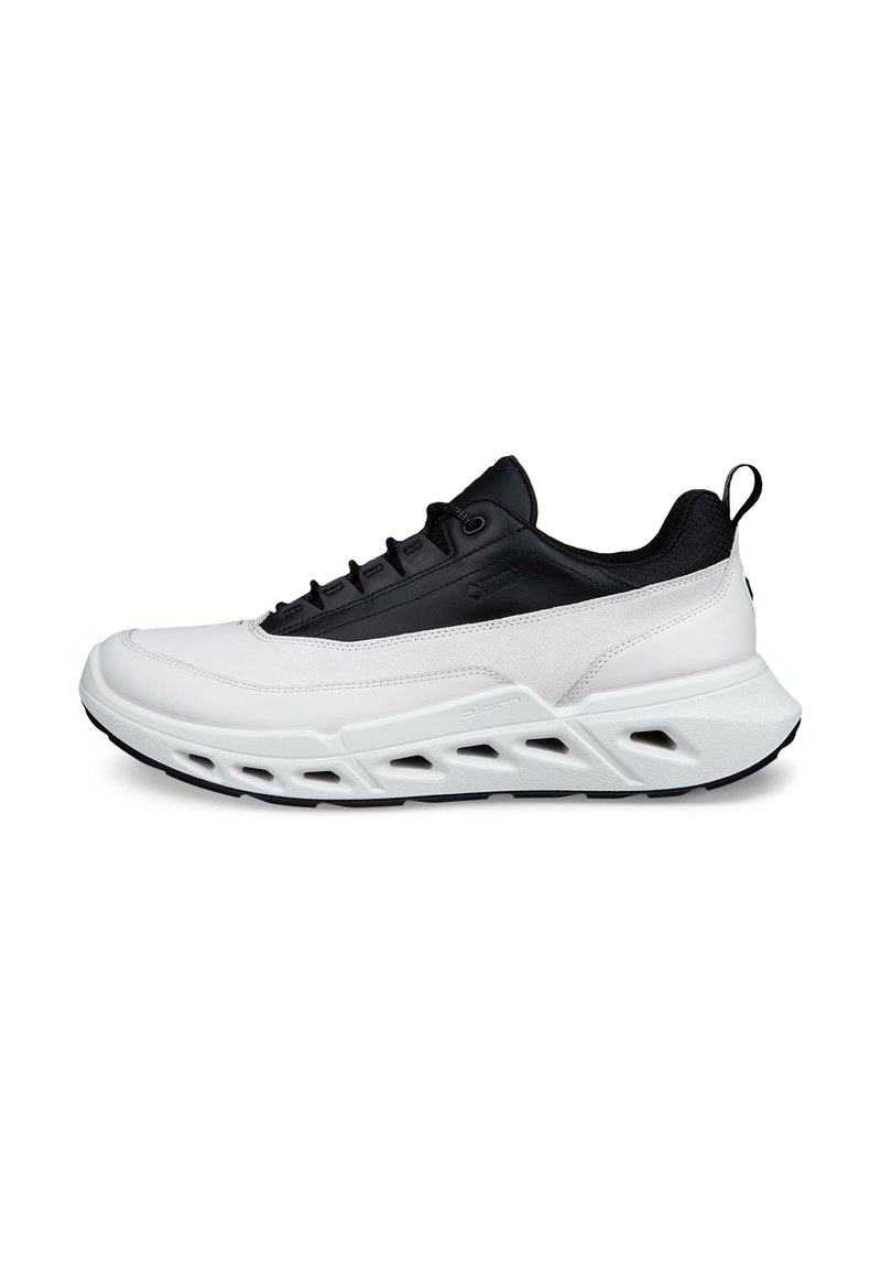 Chaussures de sport blanches et noires avec une tige synthétique, un design texturé, un système de laçage sécurisé et une semelle évidée pour la ventilation.