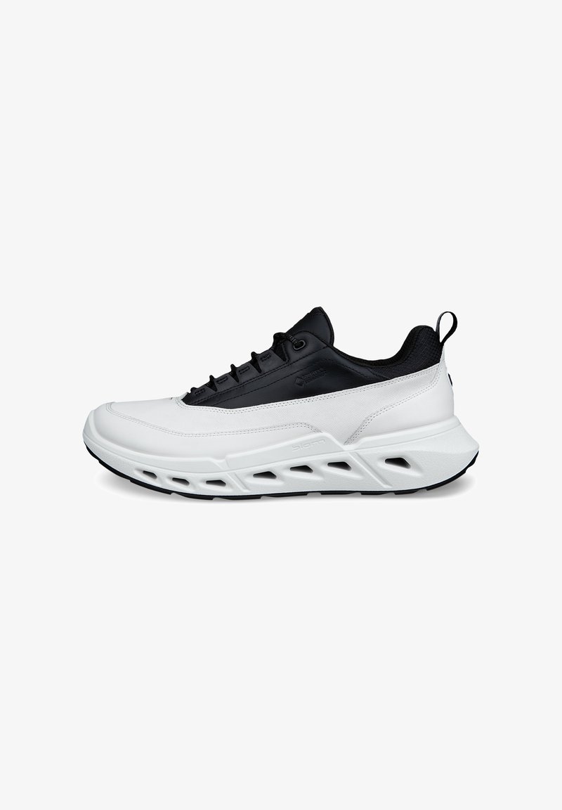 Chaussures de sport blanches et noires avec une tige synthétique, un design texturé, un système de laçage sécurisé et une semelle évidée pour la ventilation.