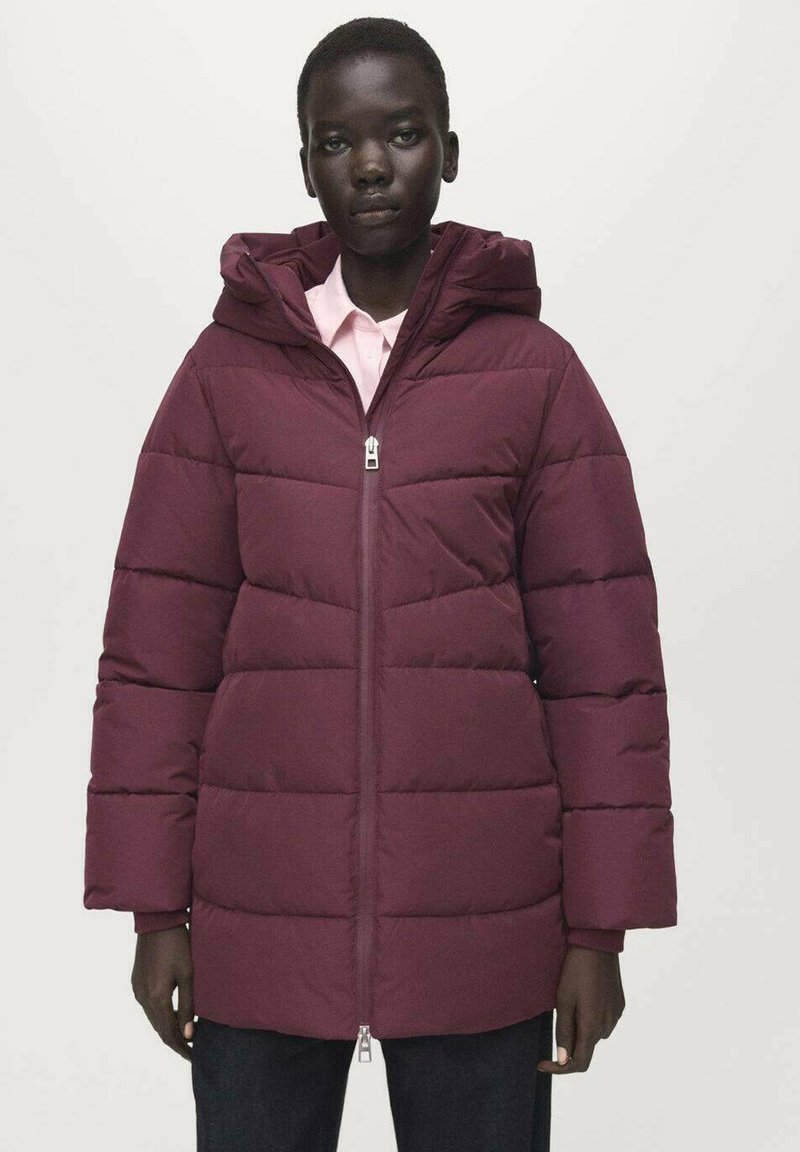 Burgundská prošívaná bunda s kapucí, s předním zapínáním na zip, vodorovným šitím a širokými rukávy. Nošena přes světle růžovou košili.