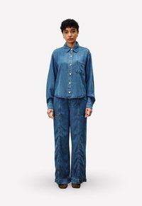 Denim overhemd met een kraag, een zak aan de voorkant en knoopsluiting, gecombineerd met loszittende denim broek, beide in een middelblauwe wassing.