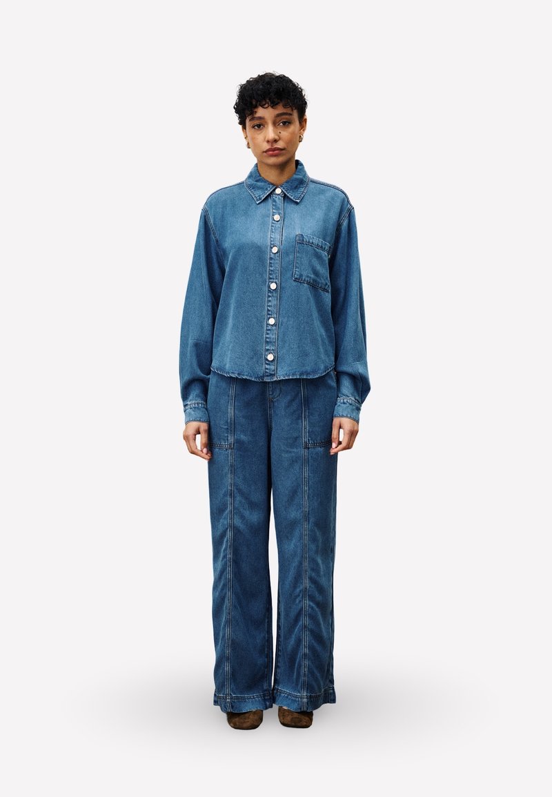 Denim overhemd met een kraag, een zak aan de voorkant en knoopsluiting, gecombineerd met loszittende denim broek, beide in een middelblauwe wassing.