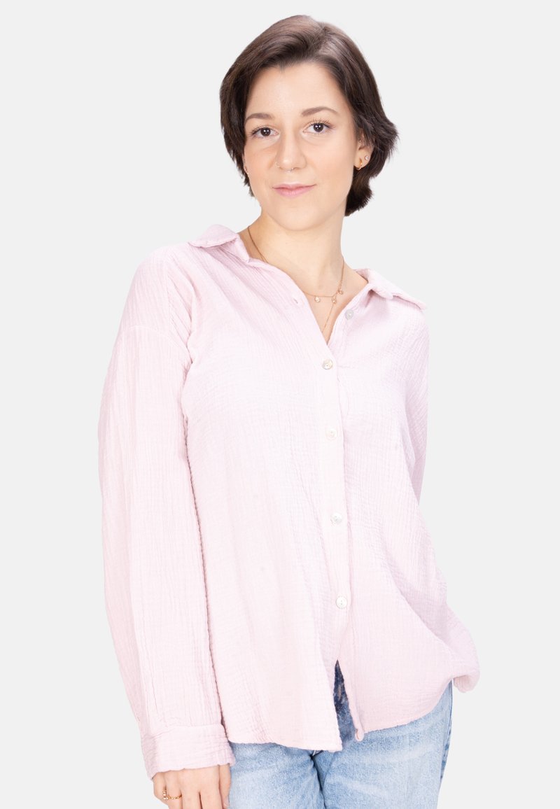 Light pink long-sleeve button-up shirt in textured fabric, featuring a collared neckline and slightly curved hem, paired with denim jeans.