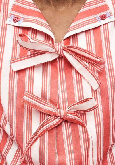 Κόκκινο και άσπρο μπλούζα με κάθετες ρίγες, με δύο δεμένα φιόγκους μπροστά και κεντητές λιβελούλες κοντά στα κουμπιά του γιακά.