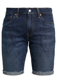 Tummansiniset farkkushortsit, joissa on revitty helma ja klassinen viiden taskun muotoilu kuparisella varusteilla ja kirjailtulla yksityiskohdalla.