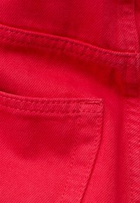 Gros plan sur un tissu denim rouge vif montrant des coutures détaillées le long du bord d'une poche.