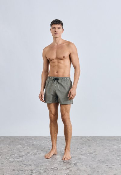 Ριγέ μαγιό βερμούδα σε πράσινο και μπεζ, κατασκευασμένο από ελαφρύ ύφασμα. Ελαστική μέση με κορδόνι, διαθέτει πλαϊνές τσέπες, με μήκος μέχρι το γόνατο.