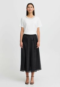 T-shirt bianco a maniche corte con scollo impreziosito, abbinato a una gonna maxi nera plissettata. La gonna presenta una vita elasticizzata e un sovrapposto trasparente.