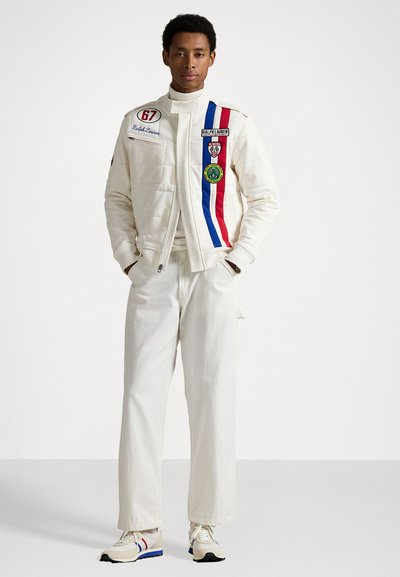 White padded jacket with red, blue, and white stripes, multiple patches, high collar; paired with white pants and beige sneakers.