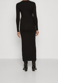 Svart, långärmad maxiklänning med en figursydd silhuett, tillverkad av ett mjukt tyg. Klänningen har en rund hals och kombineras med svarta klackstövlar.