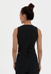 Black pinstripe sleeveless top with a high neckline and a small bow detail at the back, made from a smooth fabric with a tailored fit.