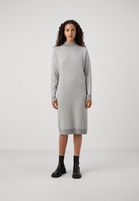 Robe en tricot grise avec un motif géométrique, col montant, manches longues et poignets côtelés, associée à des bottines noires.