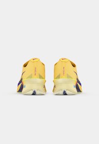 Baskets de course jaunes avec une tige en maille texturée, des accents violets et un design de semelle distinctif. Logo sur le talon et les côtés.