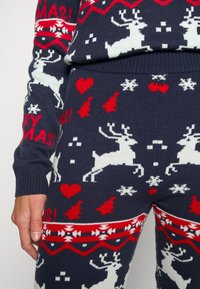 Julmönstrad stickad lounge-set i mörkblått, med vita renar, röda hjärtan och snöflingor. Mjuk, texturerad tyg med ribbade muddar.