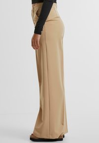 Beige high-waisted wijde broek gemaakt van een soepele stof, met een op maat gemaakte pasvorm, zijzakken en een schoon, minimalistisch ontwerp.