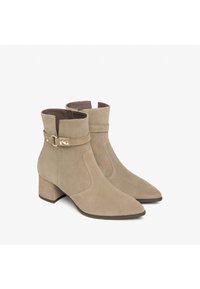Bottines en suède beige avec un bout pointu et un talon bloc. Présente une sangle décorative avec une boucle métallique en accent.