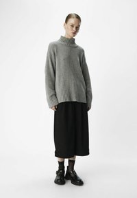 Pull à col roulé côtelé gris, coupe décontractée, associé à une jupe midi noire et des chaussures noires. Texture lisse, design simple, contraste de couleurs subtil.