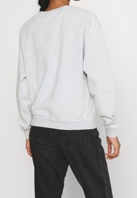Felpa grigia chiara con scollo a girocollo e polsini a costine. Presenta una vestibilità rilassata e una morbida texture del tessuto, abbinata a jeans scuri.