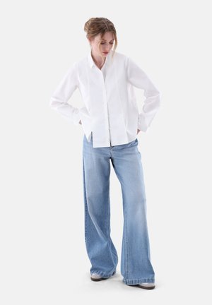 Camicia bianca con colletto e maniche lunghe, abbinata a jeans blu chiaro a gamba larga. Tessuto morbido, vestibilità casual, senza motivi visibili.