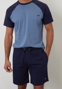 Kurzärmliges T-Shirt in Hellblau mit Marineblauem Raglanärmel, kombiniert mit Marineblauen Shorts mit elastischem Bund und seitlichen Taschen.