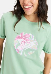 Mintgrøn kortærmet T-shirt med et cirkulært blomstermønster i pink, blå og gul, med et hjerte-design i midten.