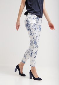 Pantalones estampados florales en blanco y azul con un corte ajustado. Presentan una tela texturizada y un diseño de tiro medio. Combinados con tacones altos en color marino.