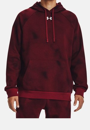 Homme portant un sweat à capuche texturé rouge foncé avec une poche avant et le logo blanc Under Armour sur la poitrine, associé à un pantalon assorti.
