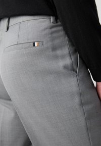 Gray tailored pants with a subtle texture, featuring a back pocket with a decorative stripe in black, white, and tan.