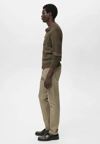 Brun ribbad kappa, beige byxor och svarta loafers. Sidoprofilvy som visar upp den texturerade tyget och knappdetaljer. Enkelt design.