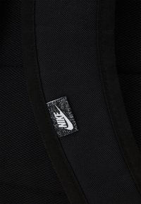 Black fabric featuring a textured surface with a Nike label in white, showing a swoosh logo and contrasting black background.