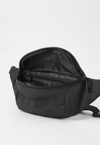 Marsupio in nylon nero con scomparto principale dotato di chiusura a zip e tasca interna con zip. Cinturino texturizzato per la regolazione.