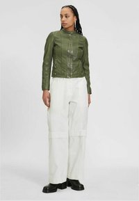 Grüne Lederjacke mit Reißverschluss vorne und Seitentaschen, kombiniert mit weißen weit geschnittenen Hosen und schwarzen klobigen Stiefeln. Glatte Textur, taillierte Passform.