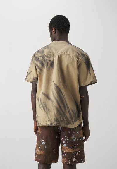 T-shirt med korte ærmer i tan farve i bomuld med sorte tie-dye mønstre, parret med brune shorts med farverige sprøjt. Casual, afslappet pasform.