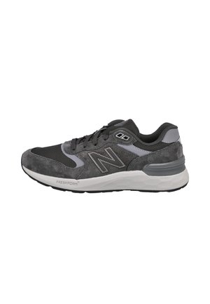 Zapatilla New Balance gris y negra con parte superior de malla y ante, suela blanca acolchada y logo lateral bordado, vista desde el lado exterior.