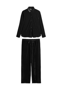 Schwarzes Velourshemd mit langen Ärmeln und kontrastierendem Lederkragen, kombiniert mit passenden schwarzen Velourshosen mit verstellbarem Bund. Weiche Textur im gesamten Outfit.