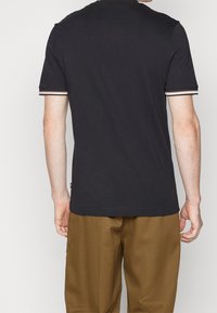 Marineblauw T-shirt met korte mouwen en witte en rode gestreepte accenten op de kraag en mouwzomen. Zachte katoenen stof. Standaard pasvorm.