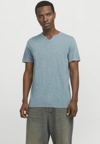 Lys blå kortærmet t-shirt med henley-udskæring og to knapper, lavet af et tekstureret, let strækbart stof.