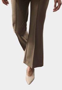 Beige flared broek met een gladde textuur en een nauwsluitende taille, gecombineerd met puntige nude hakken, wat zorgt voor een elegante, verlengde uitstraling.
