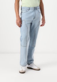 Lichtblauwe denim jeans met een recht figuur, zichtbare naden en twee voorzakken. Gekleed met witte en beige sneakers.