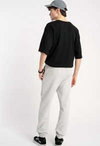 Czarna, oversize koszulka, szare dresowe spodnie i czarne sneakersy. Koszulka ma okrągły dekolt; dresowe spodnie mają boczne kieszenie i zwężane nogawki.