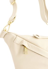 Cremfarbene Lederhandtasche mit strukturiertem Finish, goldenen Beschlägen und einem Reißverschluss. Der Tragegurt ist verstellbar und mit Nähten verziert.