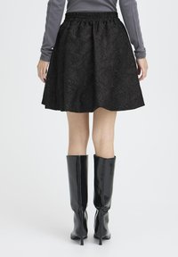 Black skirt with a textured rose pattern, elastic waistband, and a flared shape. Paired with high, glossy black knee-length boots.