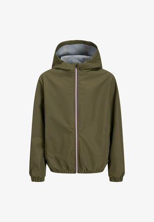 Lyshåret dreng stående iført en olivengrøn hættejakke, navyblå "Bangkok" t-shirt, løstsiddende lyseblå jeans og hvide og blå sneakers.