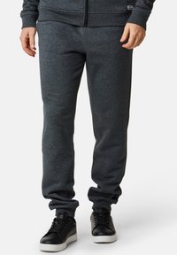 Grå bomullssweatpants med elastisk midja och muddar. Matchas med svarta sneakers med en vit sula. Minimalistisk design, inga mönster.