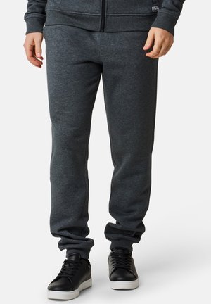 Grå bomulds sweatpants med elastisk talje og manchetter. Sammen med sorte sneakers med hvid sål. Minimalistisk design, ingen mønstre.