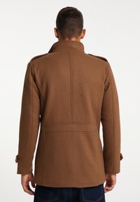 Abrigo de mezcla de lana marrón con un alto cuello, epaulettes en los hombros y un corte entallado con costuras en la parte posterior. Botones visibles como acentos en las mangas.