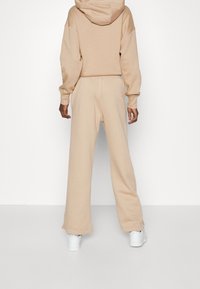 Sudadera beige y pantalones de chándal a juego, hechos de una tela suave, con un corte relajado y mangas largas, combinados con zapatillas blancas.