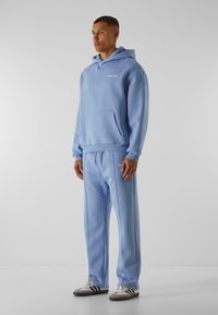 Lyseblå h�ættetrøje med lomme foran og logo, parret med matchende sweatpants med sidesyninger og snor. Casual stof.