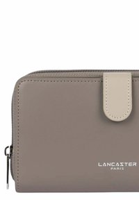 Portefeuille synthétique gris avec fermeture éclair, présentant un accent de rabat beige et le logo embossé "LANCASTER PARIS" à l'avant.