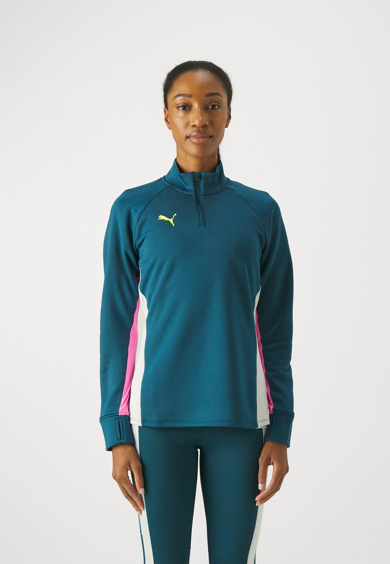 Türkiser Sporttop mit Reißverschluss und pinken sowie weißen Seitenpaneelen. Verfügt über einen hohen Kragen und lange Ärmel; hergestellt aus einem glatten, dehnbaren Stoff.